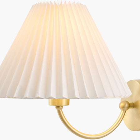 Wall-mounted lamp with pleated white shade and gold fixture on a white background