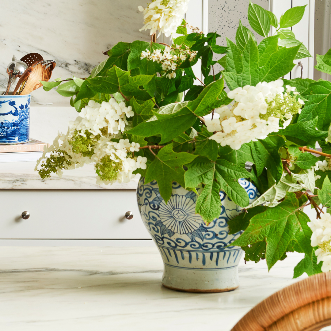 Decorative Sunnflower Temple Jar vase with white flowers and green leaves on a marble surface