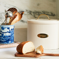Bread bin with a loaf of bread on a wooden cutting board, surrounded by kitchen utensils.