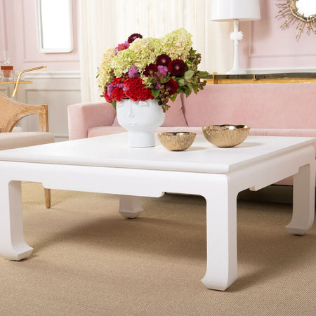 Living room with a white chow leg coffee table, pink sofa, and floral arrangement.