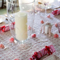 Decorative table setting with a candle in a glass holder, pink paper crackers, and a patterned tablecloth.
