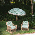 Two Rosemary Outdoor wicker chairs with green cushions and a matching umbrella in a garden setting.