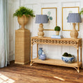 Natural Wicker Sorrento console table with lamps, vases, and plants in a room with white paneled walls.