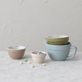 Set of colorful ceramic measuring cups on a light surface with a neutral background