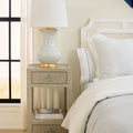 Bedroom with a nightstand featuring a lamp and decorative items, next to a bed with white bedding.